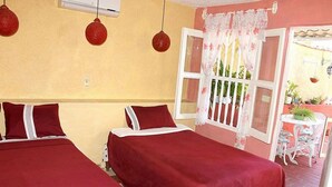 A room with two beds, a window with a white curtain, and a small table with chairs outside. - Hostal La Casa Roja TRINIDAD (Trinidad)