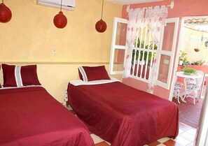 A room with two beds, a window with a white curtain, and a small table with chairs outside. - Hostal La Casa Roja TRINIDAD (Trinidad)