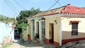 A narrow cobblestone street with buildings featuring red-tiled roofs and barred windows. - Hostal La Casa Roja TRINIDAD (Trinidad)