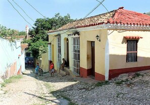 A narrow cobblestone street with buildings featuring red-tiled roofs and barred windows. - Hostal La Casa Roja TRINIDAD (Trinidad)