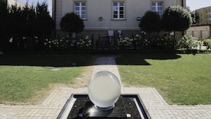 Ein Gebäude mit einer symmetrischen Fassade, einem zentralen Eingang und einem gepflasterten Innenhof mit einer kugelförmigen Skulptur.