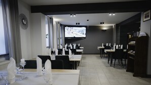 Ein Restaurant mit mehreren Essplätzen, einem an der Wand befestigten Bildschirm und einer Wanduhr.