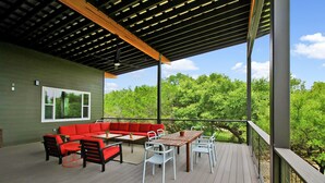 Une terrasse extérieure couverte, avec un canapé rouge, des chaises blanches et une table en bois.