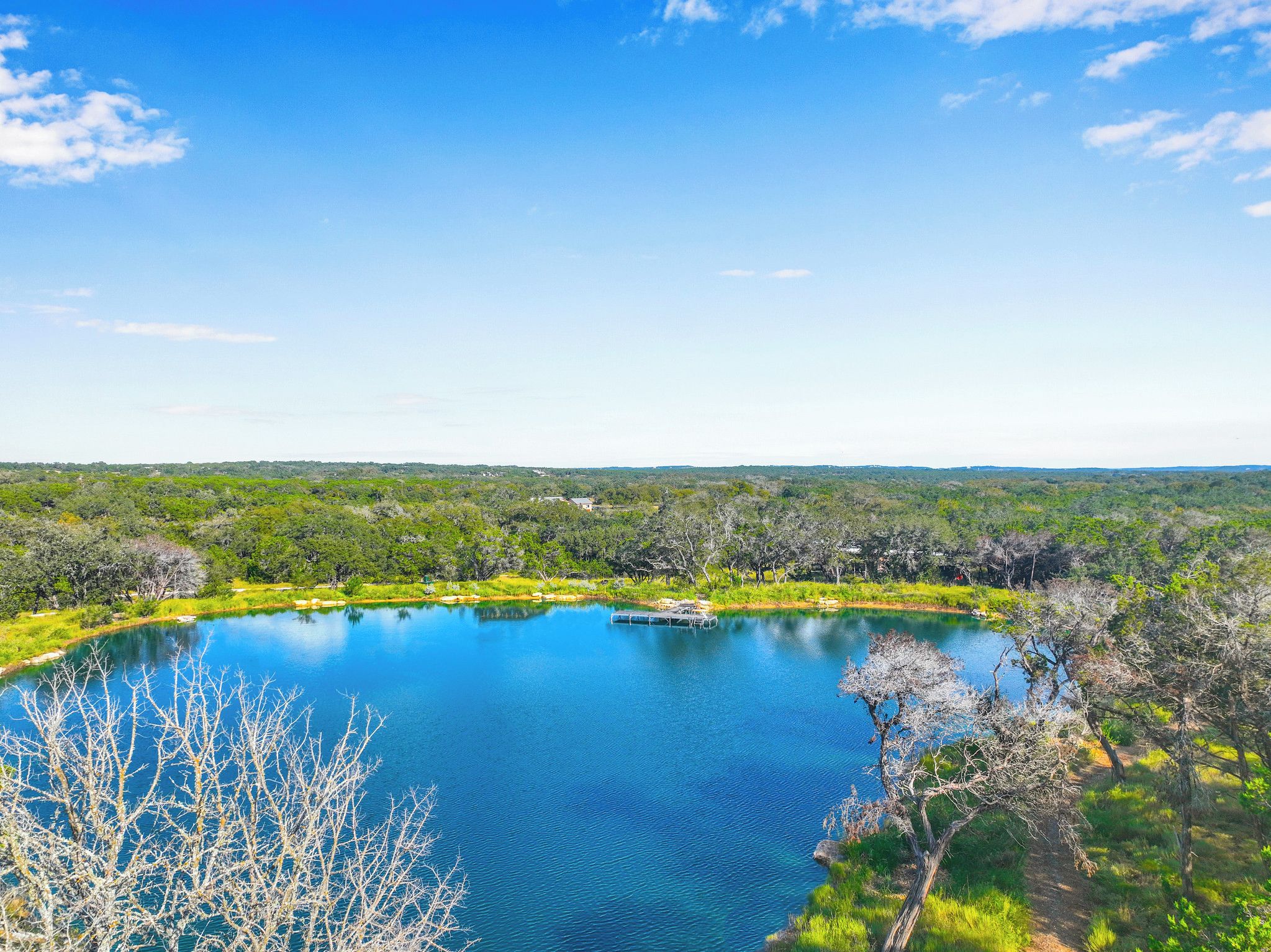 A serene lake surrounded by lush greenery and a clear blue sky.