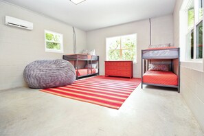 A room with two bunk beds, a red and white striped rug, a gray bean bag, and a red dresser.