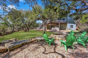 A house with a covered porch, a stone fire pit, and green Adirondack chairs. - River Road Retreat - NEW Modern 3 Bedroom on the Blanco River (Wimberley)