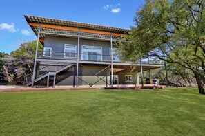 A modern two-story house with a covered patio, a staircase, and a well-maintained lawn. - River Road Retreat - NEW Modern 3 Bedroom on the Blanco River (Wimberley)