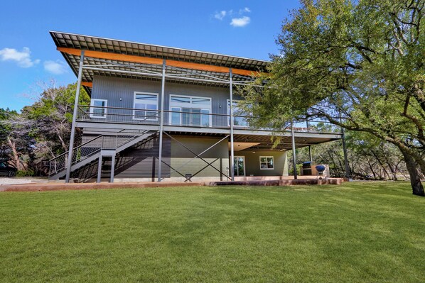 A modern two-story house with a covered patio, a staircase, and a well-maintained lawn.