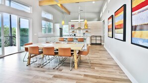 Une cuisine moderne dotée d’un îlot central, de grandes fenêtres et d’un coin repas avec une table et des chaises en bois.