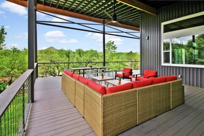 A covered outdoor seating area with wicker furniture and red cushions, overlooking a lush landscape.