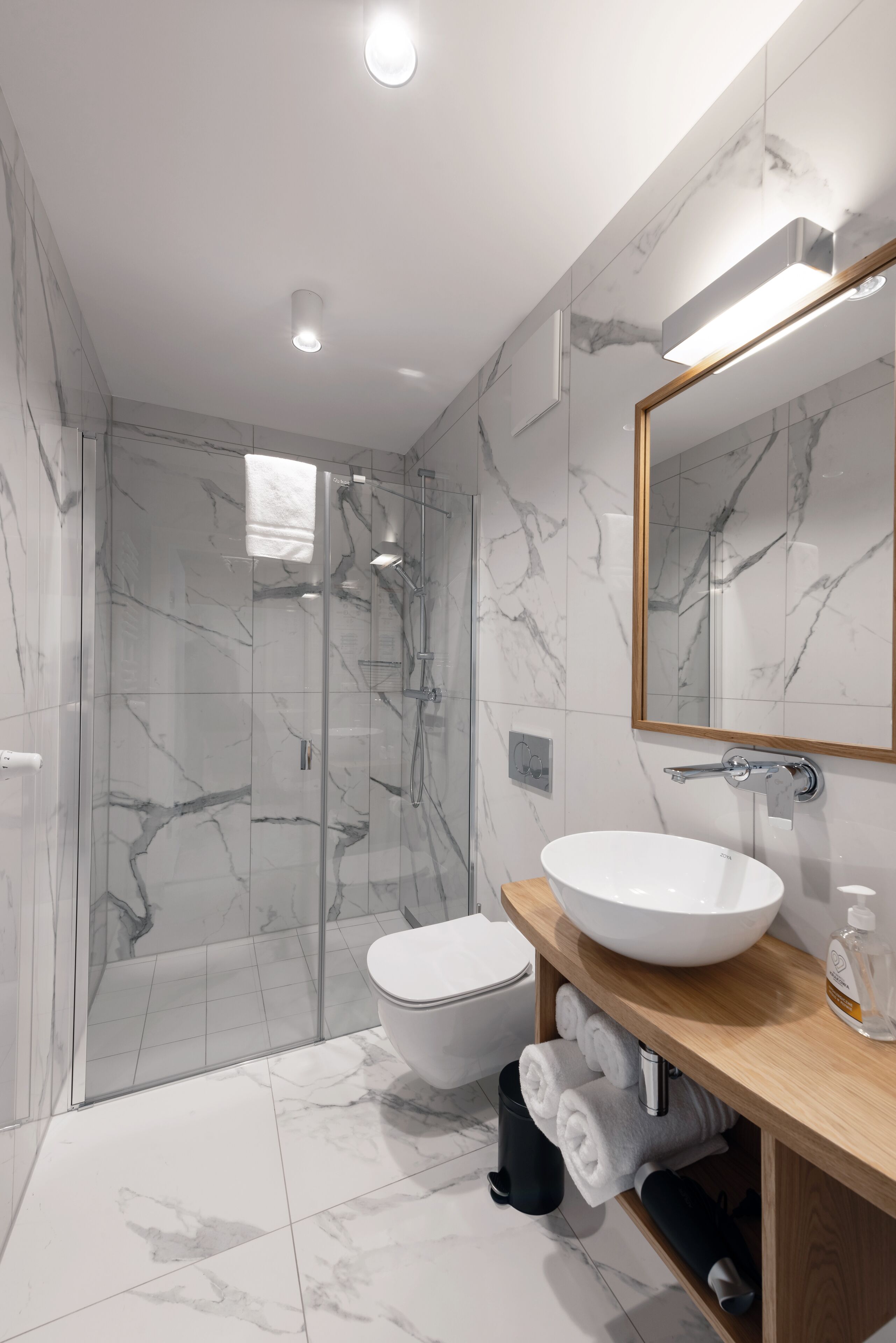 Un baño moderno con ducha envuelta en vidrio, inodoro blanco y tocador de madera con un espejo grande.