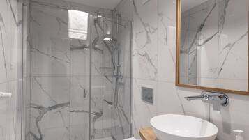 Un baño moderno con ducha envuelta en vidrio, inodoro blanco y tocador de madera con un espejo grande.
