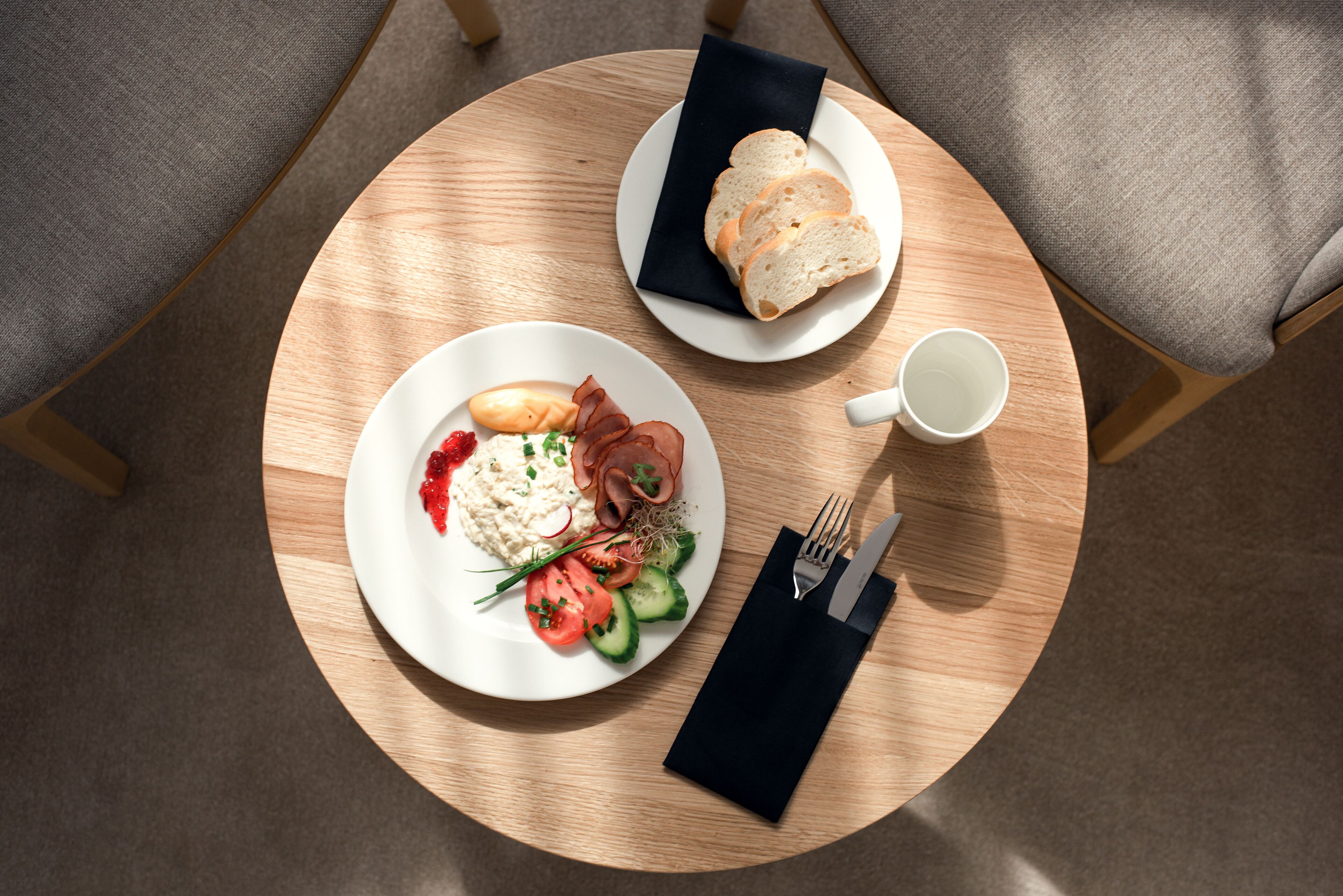 A round wooden table with a plate of food, a cup, and cutlery.