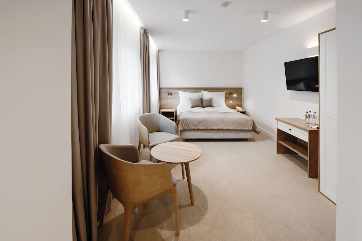 Een hotelkamer met een bed, een bureau, een stoel, een televisie en een raam met gordijnen.