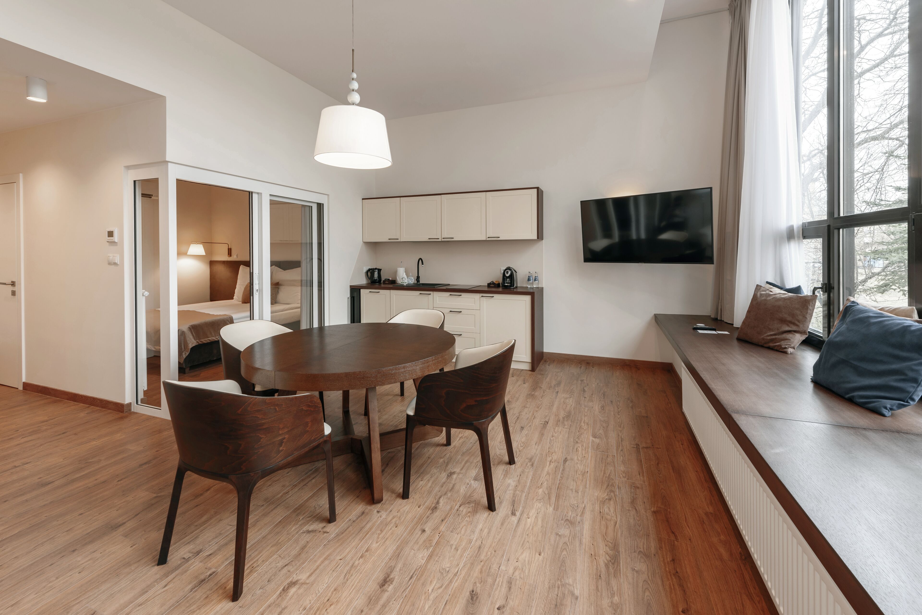 Una cucina moderna con mobili bianchi, un'area pranzo con tavolo e sedie in legno, e un'ampia finestra con vista.