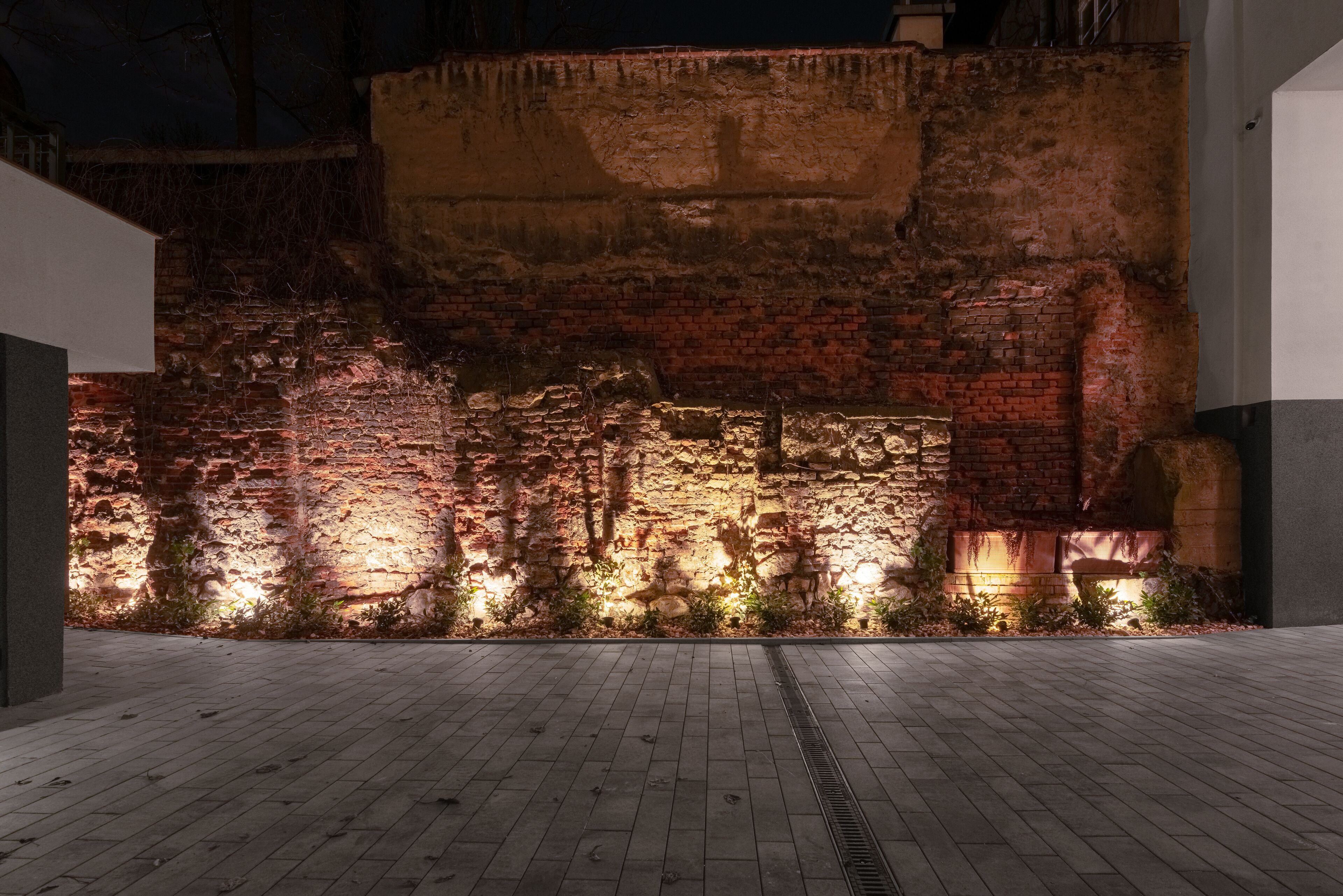 An outdoor area with a brick wall and a paved walkway.