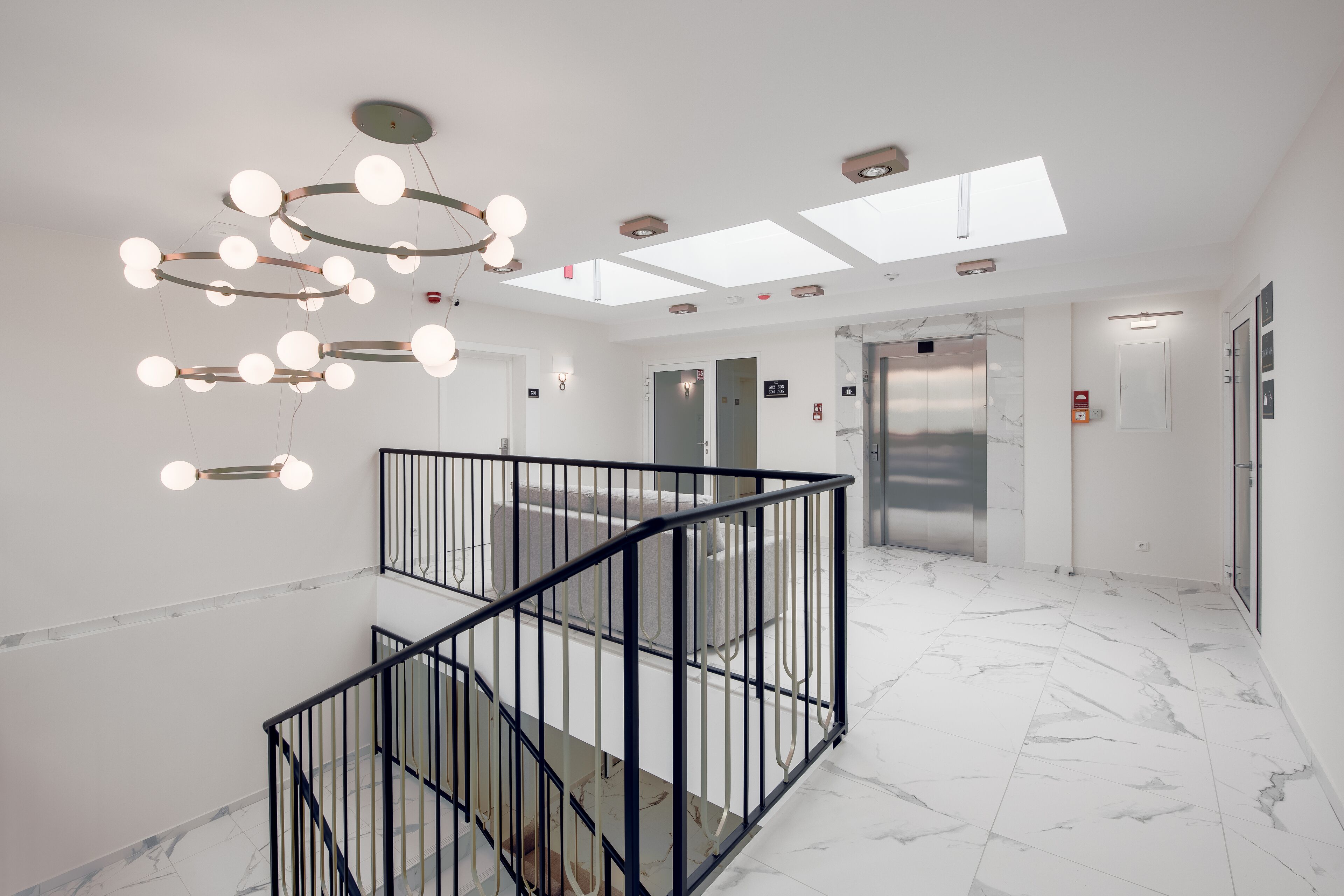 En moderne hotellobby med marmorgulv, trappe med sorte gelændere og en usædvanlig loftlampe.