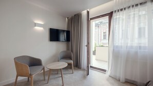 A modern room with a flat-screen TV mounted on the wall, two chairs, a small round table, and a large window with sheer curtains. - W Sercu Krakowa Aparthotel (Kraków)