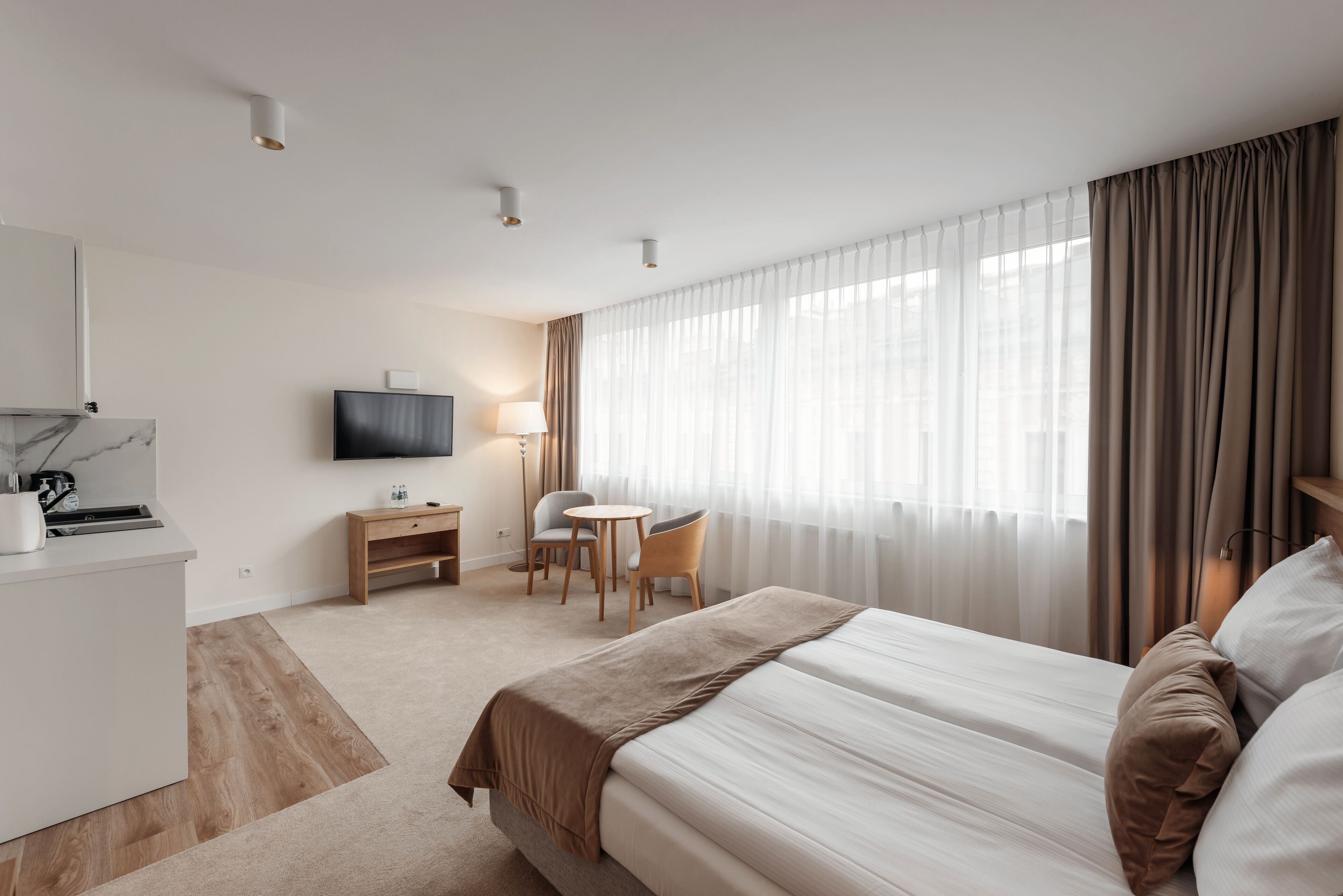 A hotel room with a bed, a desk, a chair, a TV, and a window with curtains.