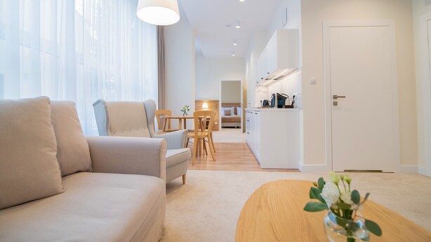 A modern living room with a sofa, a dining table, and a kitchen in the background. - W Sercu Krakowa Aparthotel (Kraków)
