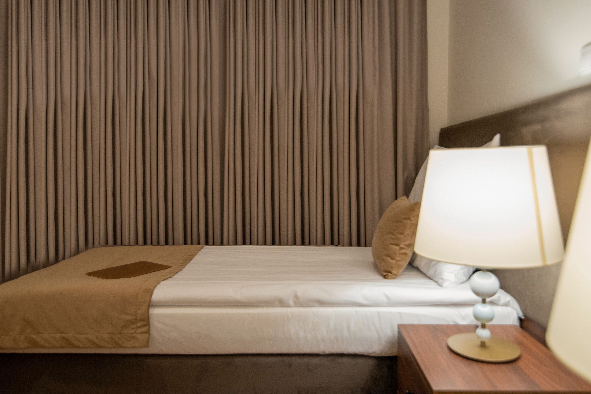 A hotel room with a bed, a nightstand, a lamp, and a curtain.