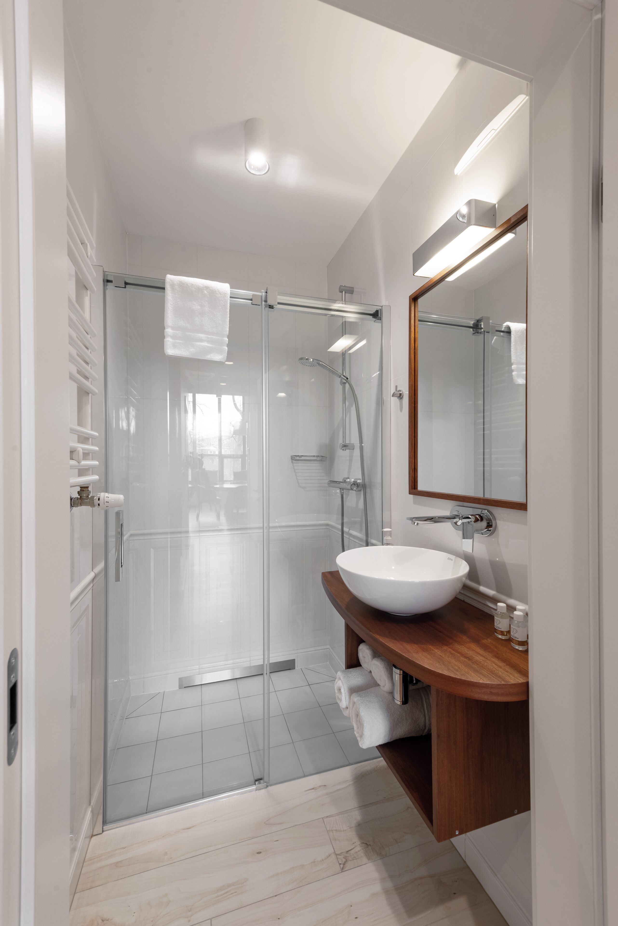 Un baño moderno con ducha envuelta en vidrio, un lavamanos blanco y un mueble de tocador de madera.