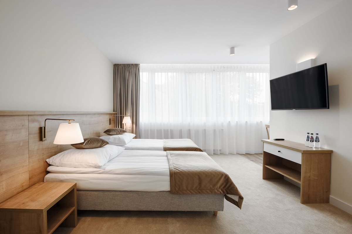 Een hotelkamer met een bed, nachtkastje, lamp, televisie en een bureau met stoel.