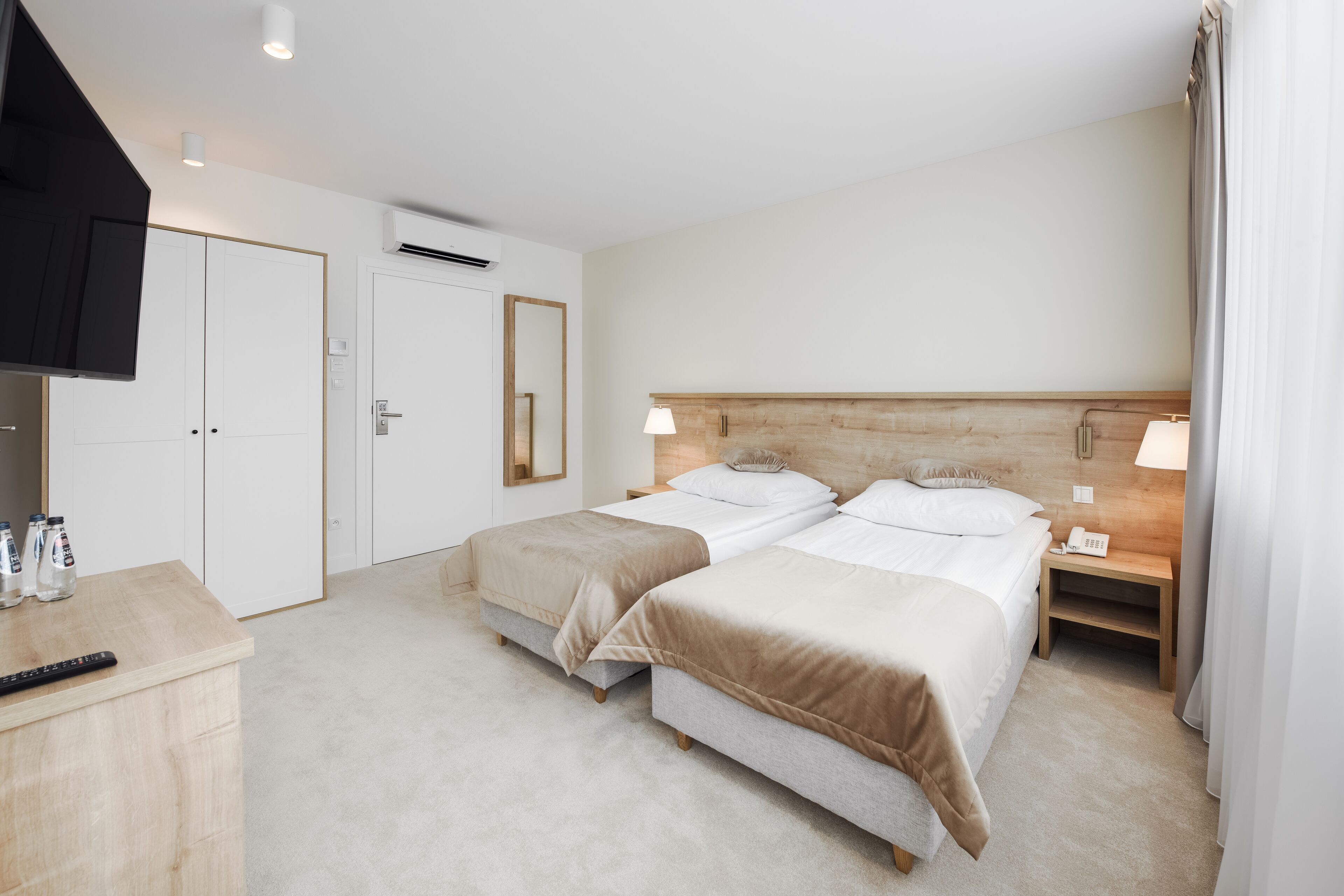 Una camera d'albergo con due letti, una TV, una scrivania e un comodino con una lampada.