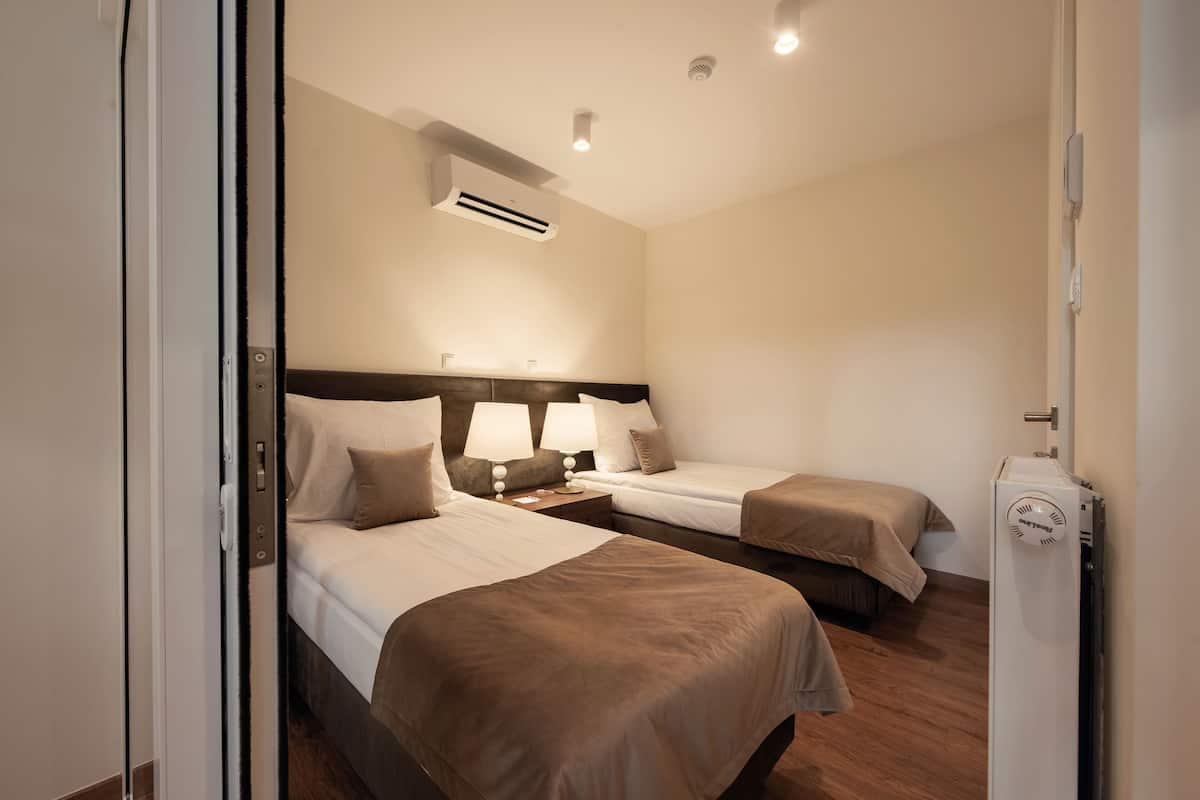 Een hotelkamer met twee bedden, nachtkastjes met lampen, een airconditioner en een thermostaat.
