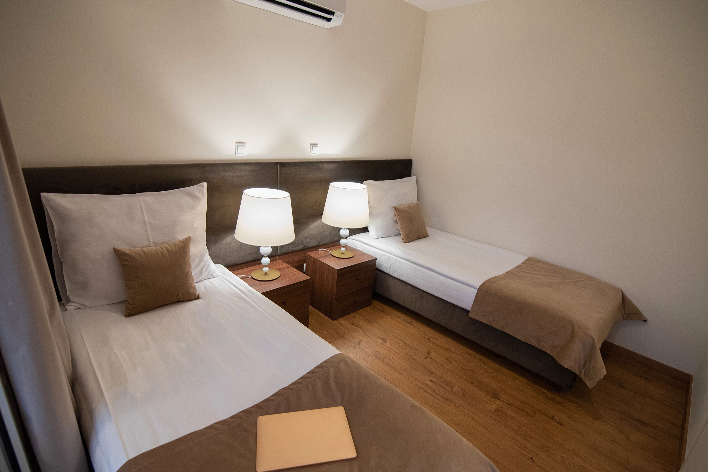 A hotel room with two beds, each with a pillow and a bedside table with a lamp.