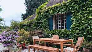 A wooden table and chairs set on a stone patio with a house covered in ivy in the background. - House in Perche (Marolles-les-Braults)