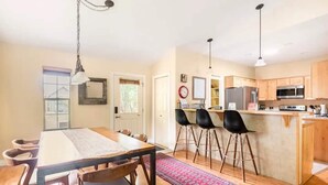 Une cuisine moderne avec des meubles en bois, un îlot central doté de tabourets, et un coin repas avec une table et des chaises.