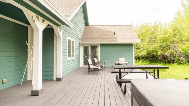Une terrasse en bois avec des meubles d’extérieur, notamment des chaises et une table, ainsi qu’une table de pique-nique couverte.