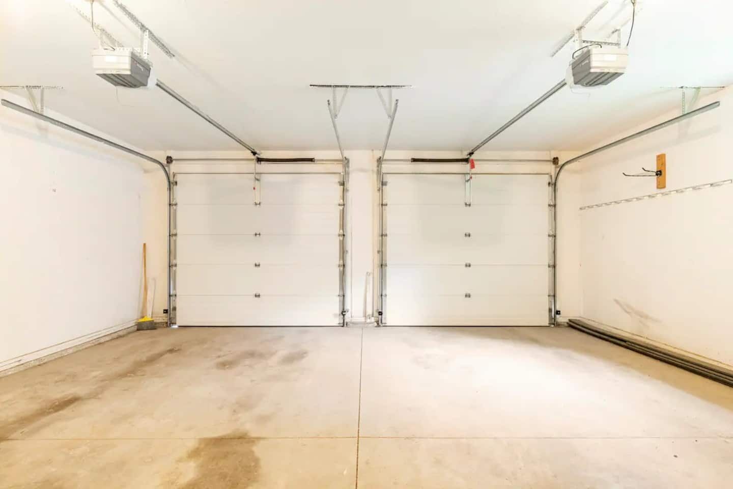 A clean, empty garage with two large garage doors, a concrete floor, and overhead lighting.