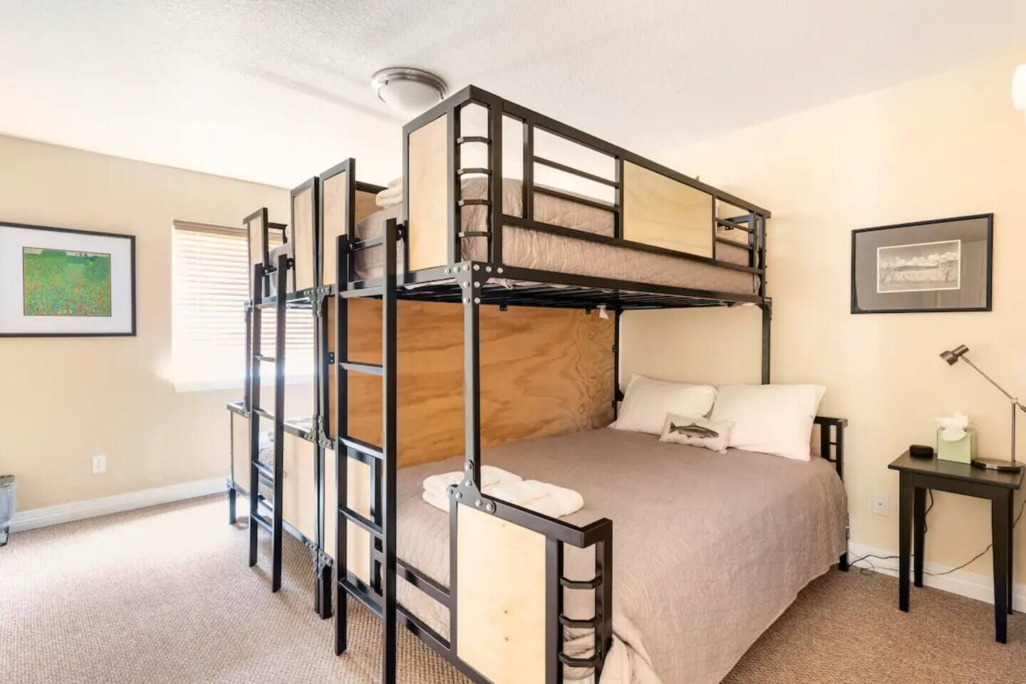 Habitación con literas, cabecera de madera, mesita de noche con lámpara y un cuadro en la pared.