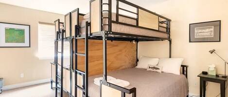 Habitación con literas, cabecera de madera, mesita de noche con lámpara y un cuadro en la pared.