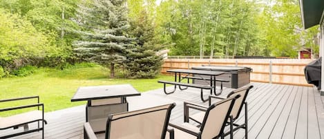 Una terraza al aire libre con mesas y sillas de picnic, rodeada de follaje y árboles.