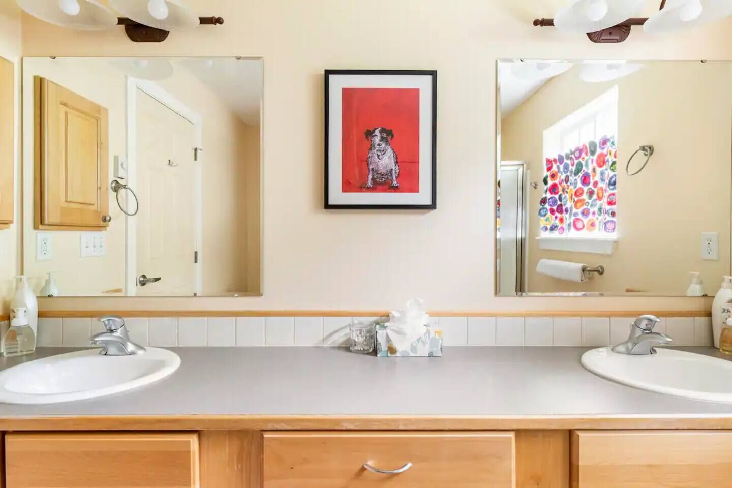 Une salle de bain avec deux lavabos, un tableau représentant un chien et un miroir au-dessus des lavabos.