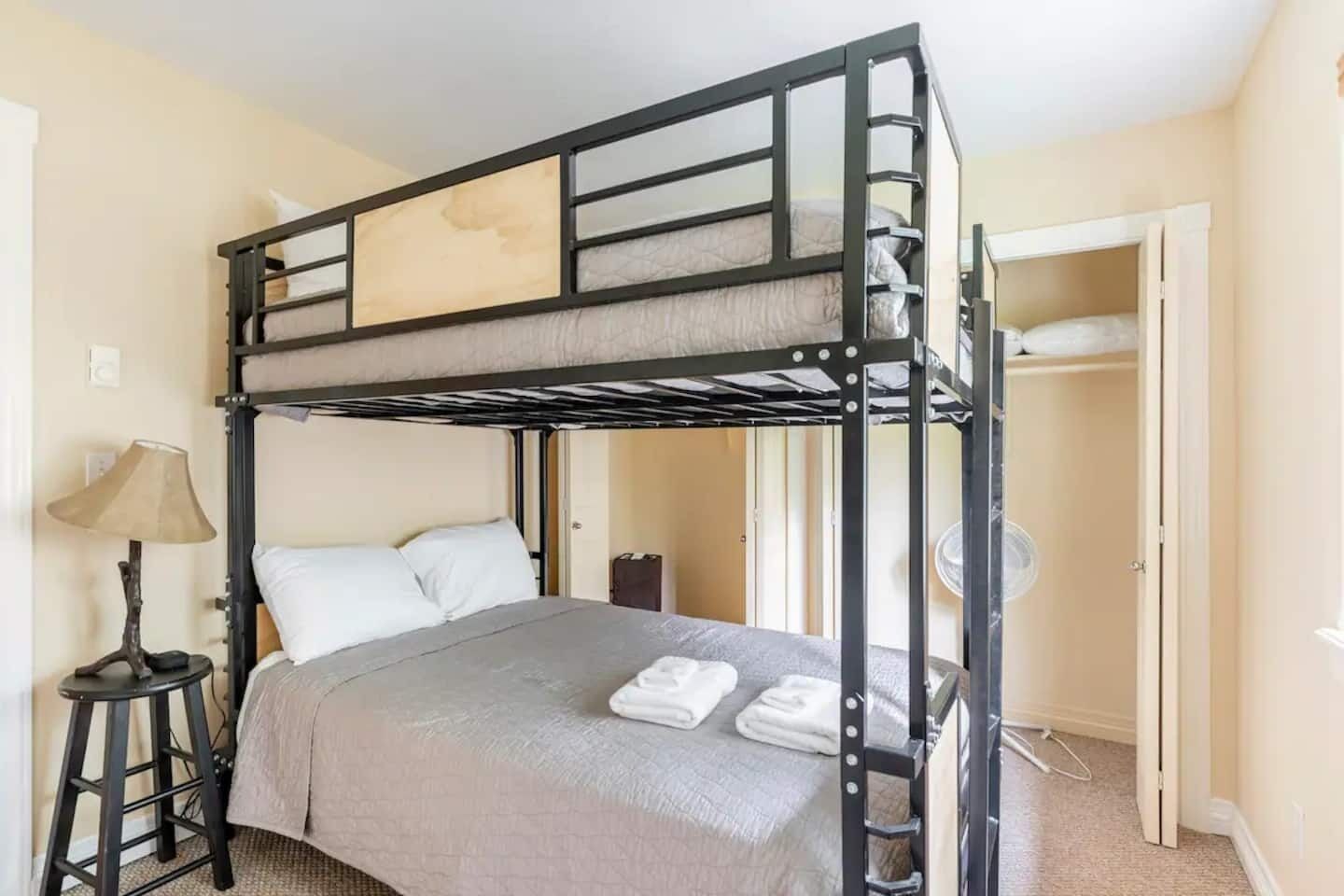 A bunk bed room with a desk and lamp, a closet, and a fan.