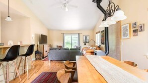 Un vaste espace de vie comprenant une table à manger en bois, des chaises noires, un canapé gris et un tapis rouge à motifs.
