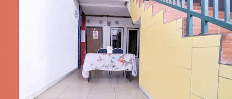 A narrow hallway with a table covered in a floral tablecloth, a door with a sign, and a staircase with a railing.