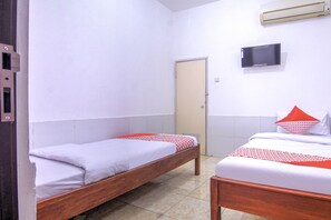 A room with two wooden beds, a television on the wall, and a door. - OYO 3317 Maju Jaya Homestay (Bogor)