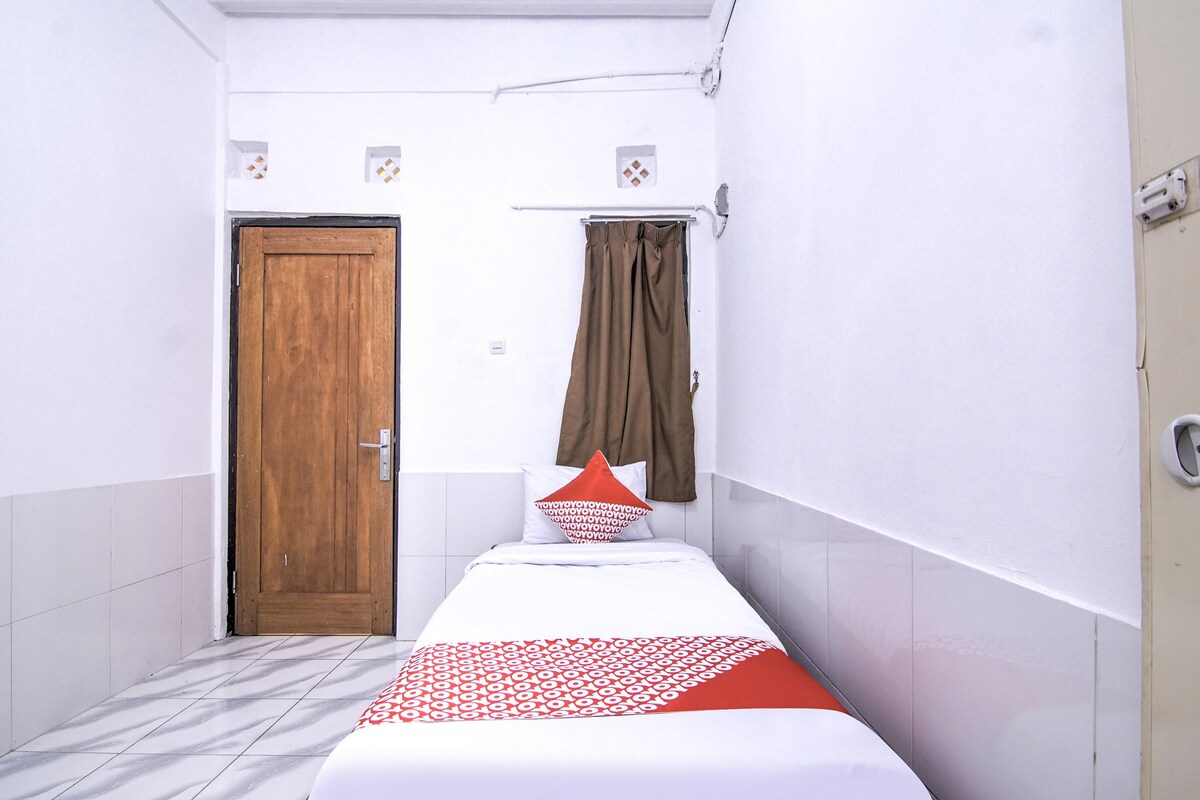 A small, narrow hotel room with a single bed, a wooden door, a curtain, and a tiled floor.
