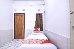 A small, narrow hotel room with a single bed, a wooden door, a curtain, and a tiled floor. - OYO 3317 Maju Jaya Homestay (Bogor)