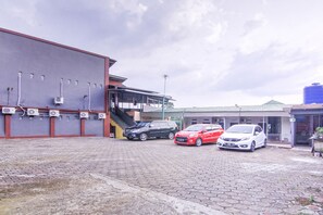 A parking area with three cars, a building with a red exterior, and a blue water tank. - OYO 3317 Maju Jaya Homestay (Bogor)