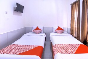 A hotel room with two single beds, each with a red and white patterned bedspread, white pillows, and a mounted television on the wall. - OYO 3317 Maju Jaya Homestay (Bogor)