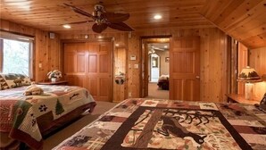 A wooden cabin bedroom with a large bed, a ceiling fan, and a quilt with animal prints. - Beautiful Back Yard with peekaboo Lake Views. Private Hot Tub & Pool Table (Big Bear Lake)