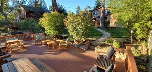 A wooden deck with outdoor furniture, a stone pathway, and a well-maintained garden. - Walk to Lake | Hot Tub, Game Room, Large Backyard & Peekaboo Lake Views (Big Bear Lake)