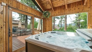 A wooden cabin with a hot tub, patio furniture, and large windows overlooking a forested area. - Beautiful Back Yard with peekaboo Lake Views. Private Hot Tub & Pool Table (Big Bear Lake)