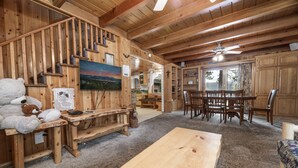 A wooden interior with a dining area, a staircase, and a painting on the wall. - Beautiful Back Yard with peekaboo Lake Views. Private Hot Tub & Pool Table (Big Bear Lake)